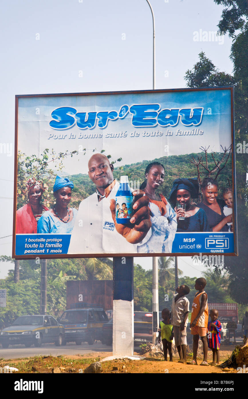 I bambini guardano fino a una pubblicità tramite Affissioni Sur Eau su una strada trafficata attraverso la Guinea la capitale Conakry. Foto Stock