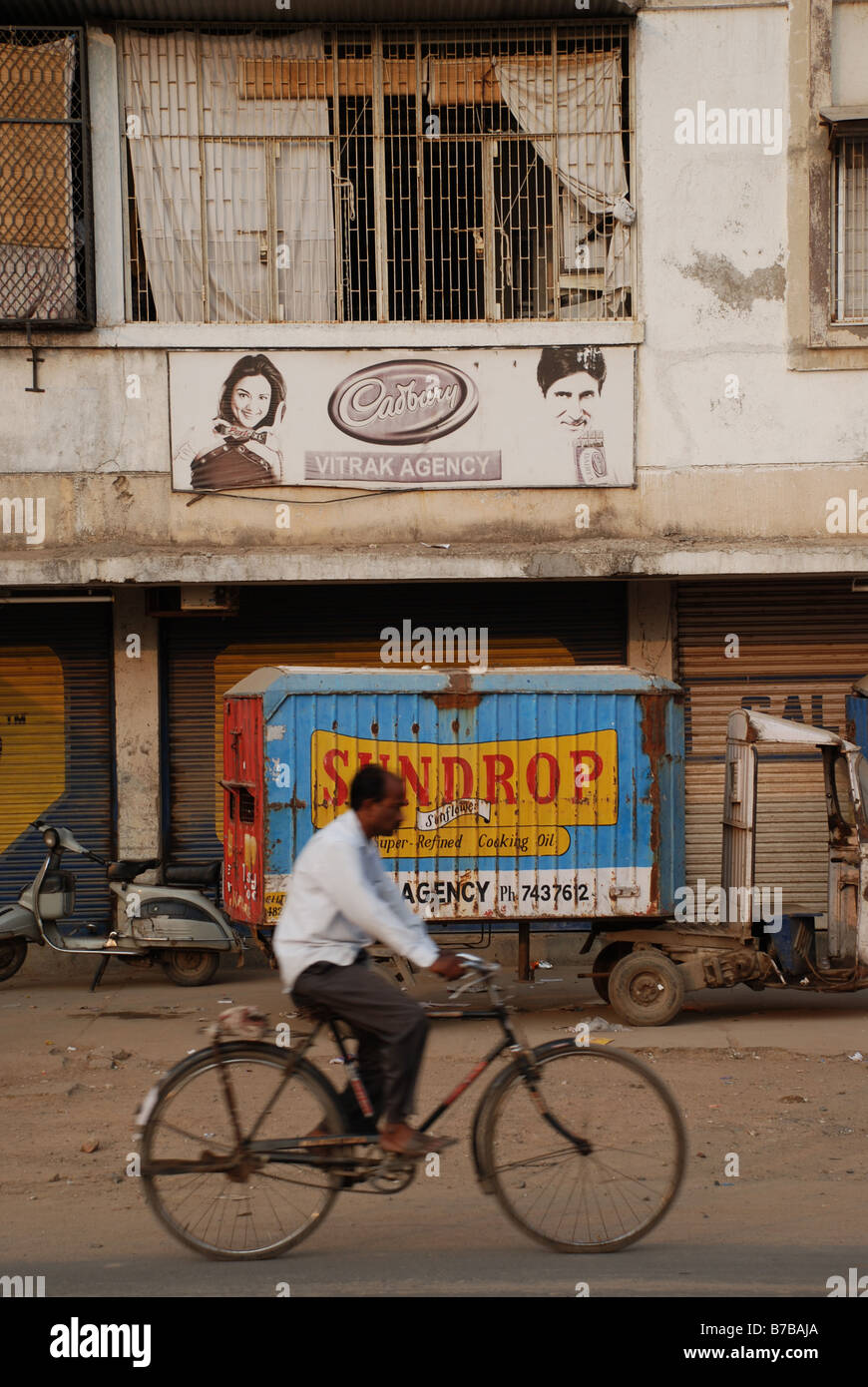 L'uomo ciclismo su strada oltre billboard aggiungere, Ahmedabad, India. Foto Stock