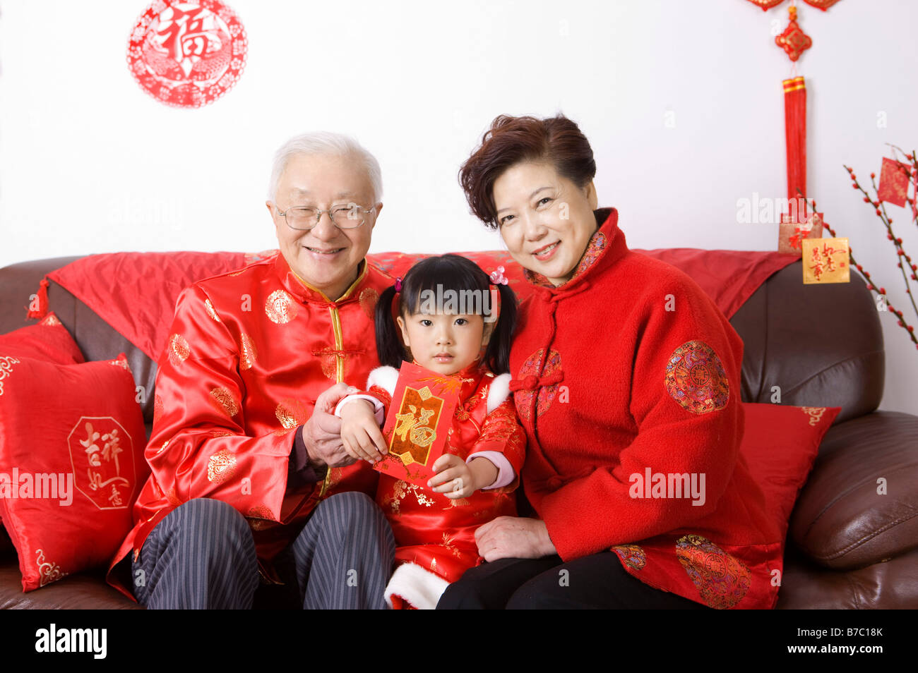 Coppia di anziani e una bambina in abiti tradizionali seduti sul divano e sorridente alla fotocamera Foto Stock