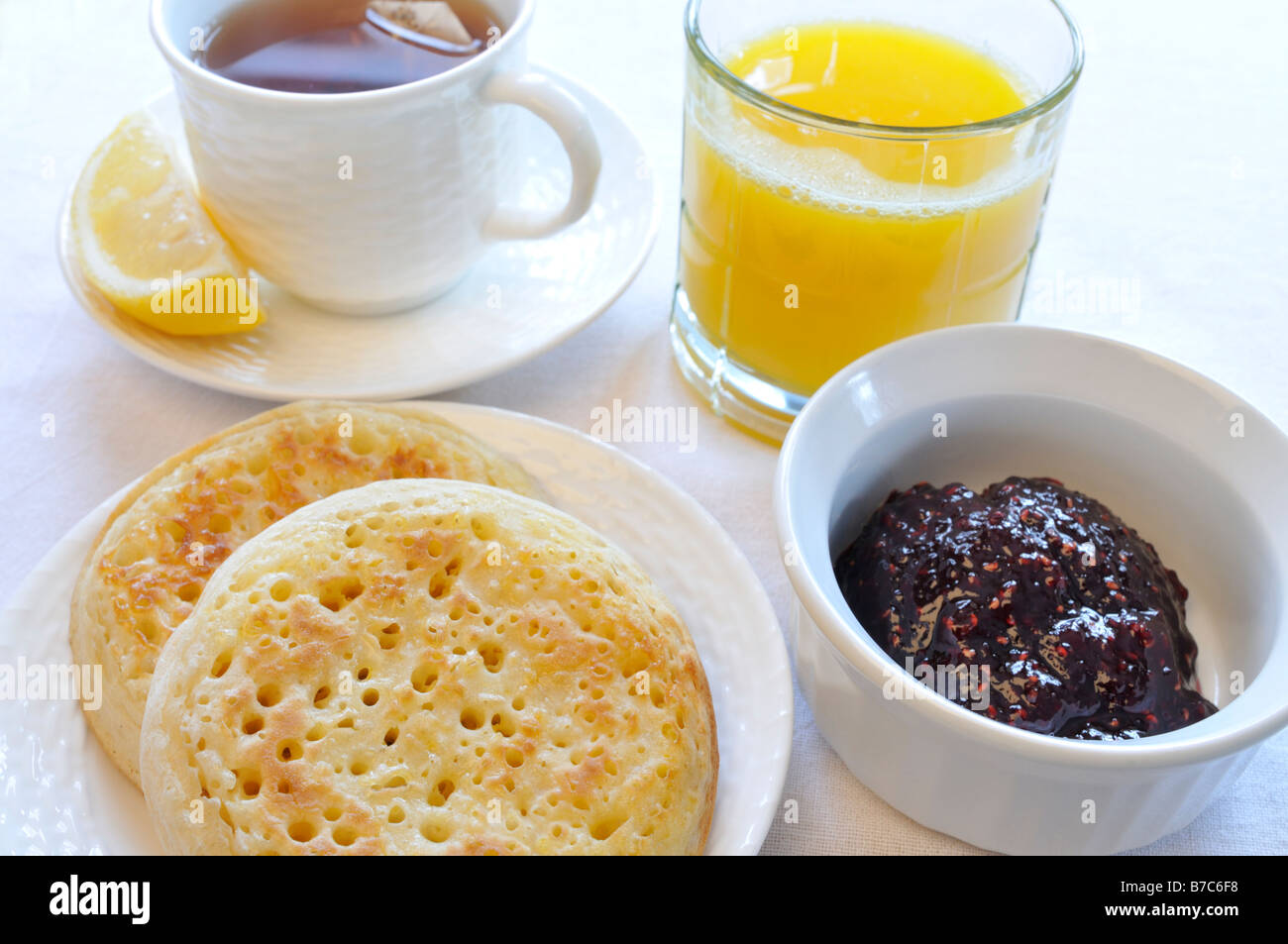 Una tazza di tè nero con limone, cialdine, marmellata e un bicchiere di succo di arancia su uno sfondo bianco. Foto Stock