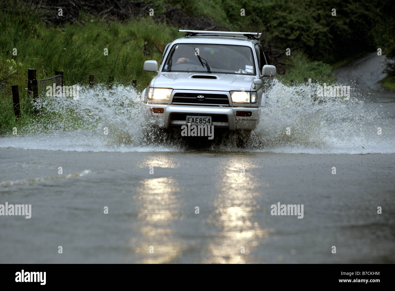 Auto con i fari accesi aziona attraverso l'acqua di allagamento sulla strada di Nelson Nuova Zelanda Foto Stock