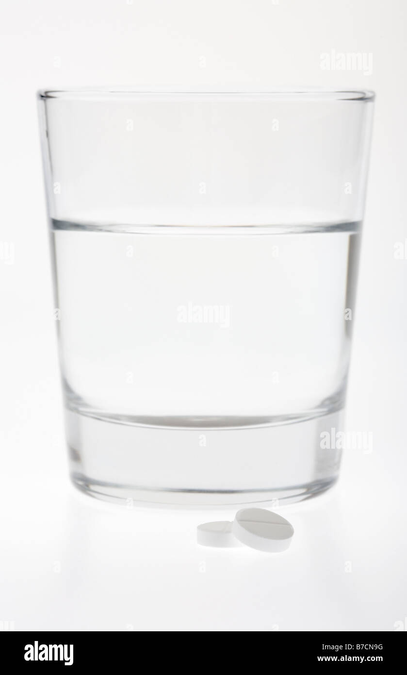 Bicchiere mezzo pieno vuoto con acqua con due compresse di paracetamolo isolati su sfondo bianco Foto Stock