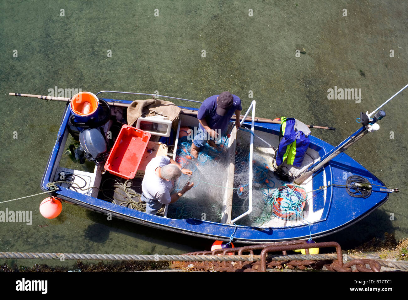 Un overhead shot il peering in un Cornish barca da pesca pescatori come riparare le loro reti da parte della parete del porto Foto Stock