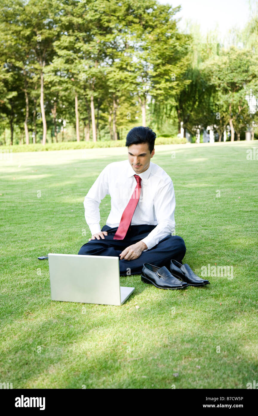Un business uomo seduto sul prato e guardando il laptop Foto Stock