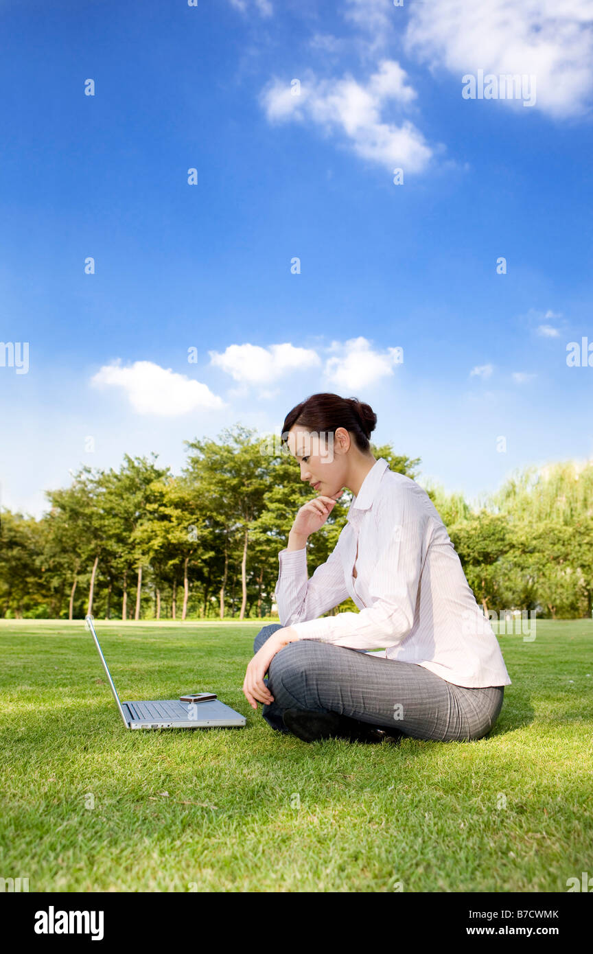 Un business donna seduta sul prato e guardando il laptop Foto Stock