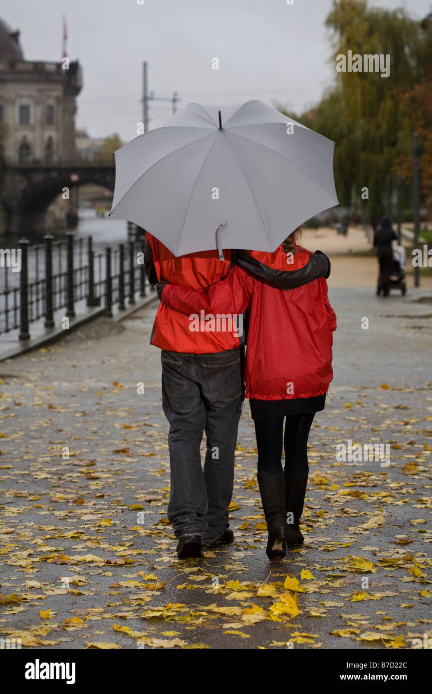 Vista posteriore di una coppia giovane a piedi con un ombrello Foto Stock