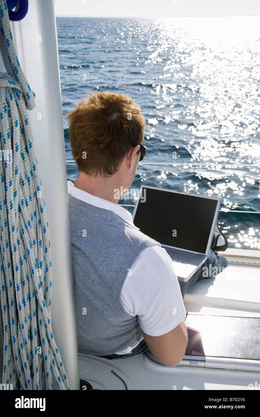 Vista posteriore di un uomo che utilizza un computer portatile su un yacht Foto Stock