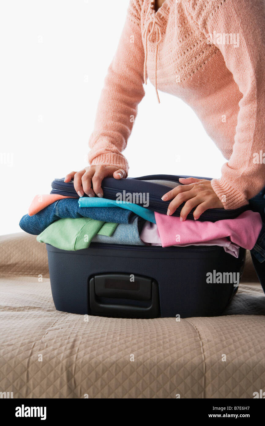 Una donna premendo su una valigia piena di vestiti Foto Stock