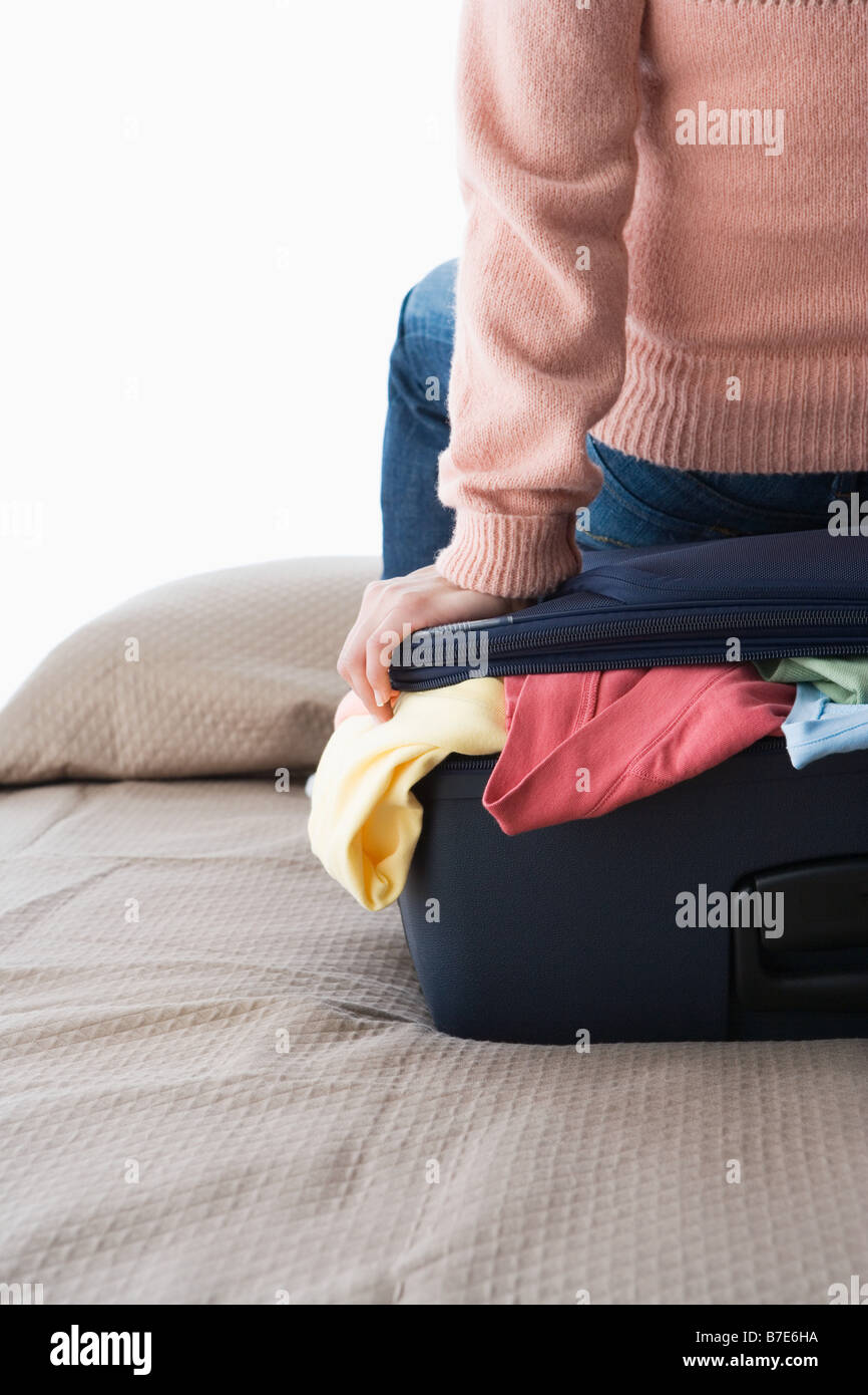 Una donna seduta su una valigia piena di vestiti Foto Stock