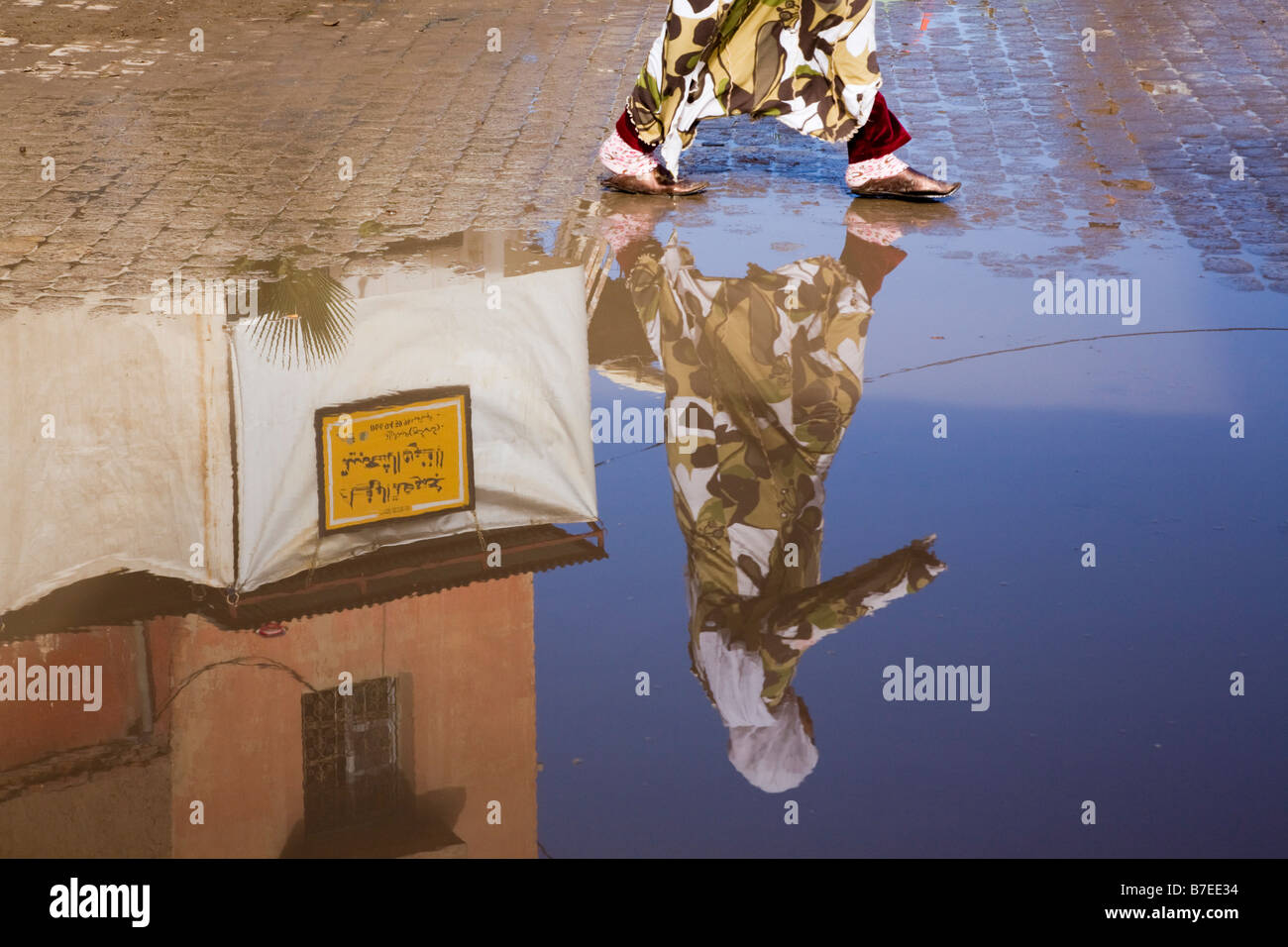 Donna marocchina a camminare in abito tradizionale riflesso in una pozza d'acqua sul terreno. Marrakech marocco Africa del Nord Foto Stock