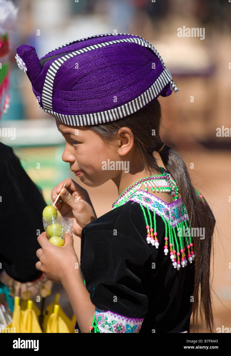 Una ragazza Hmong in costume tradizionale è mangiare un dolce su un bastone in un Hmong Anno Nuovo cerimonia. Foto Stock