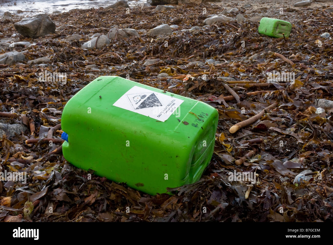 Contenitore chimici corrosivi con il simbolo di avvertimento lavato fino sulla coperta di alghe marine beach. Foto Stock