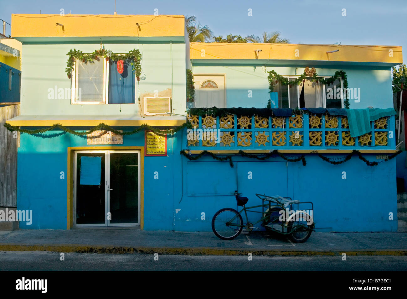 Parcheggiato a tre ruote carrello sul marciapiede davanti ad un blu edificio festosa nel dicembre su Isla Mujeres, Messico. Foto Stock