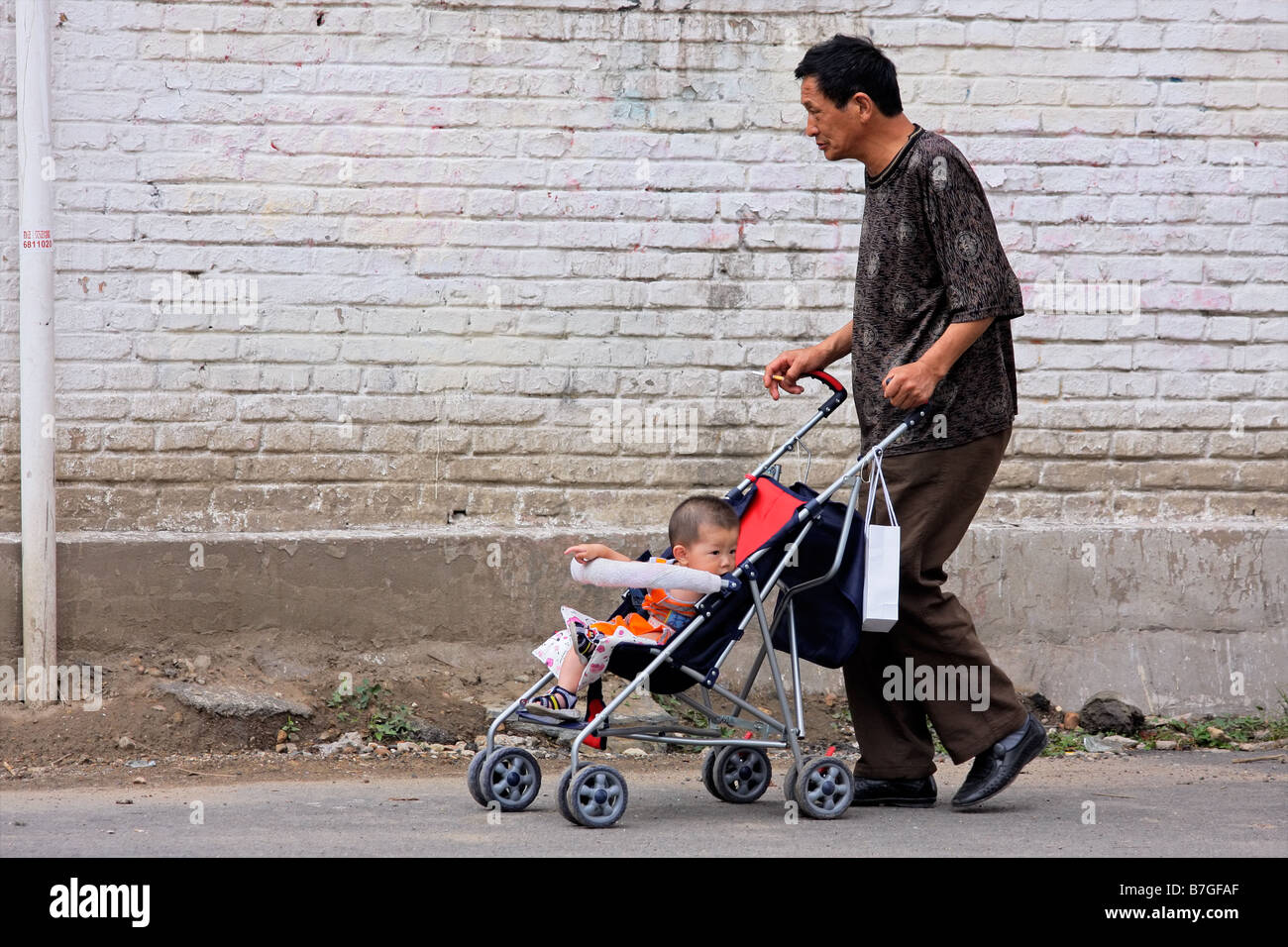 Un uomo cinese di spingere un passeggino con un bambino in strada di HoHot, Mongolia Interna, nel nord della Cina Foto Stock