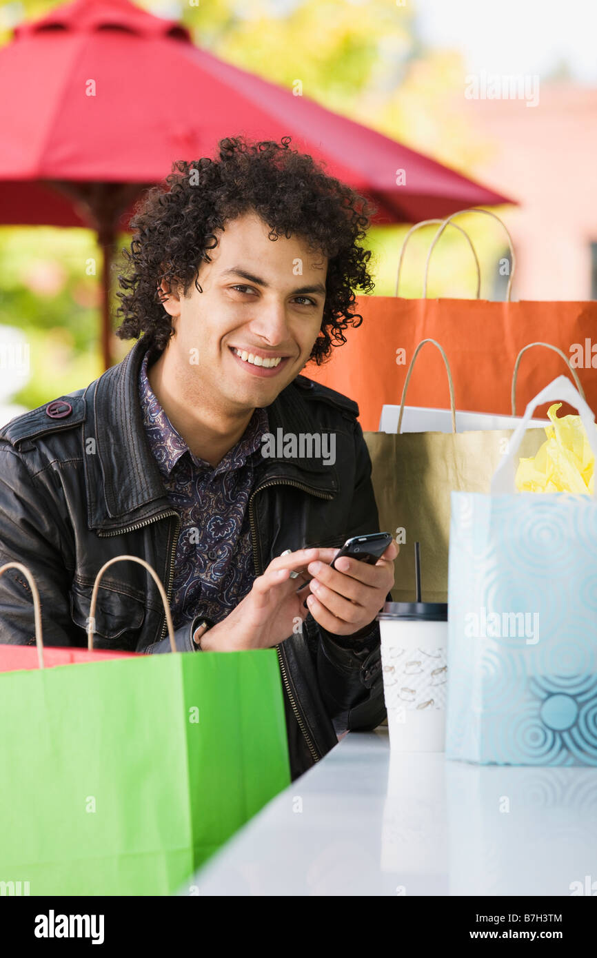 Medio Orientale con uomo borse per lo shopping di messaggistica di testo sul telefono cellulare Foto Stock