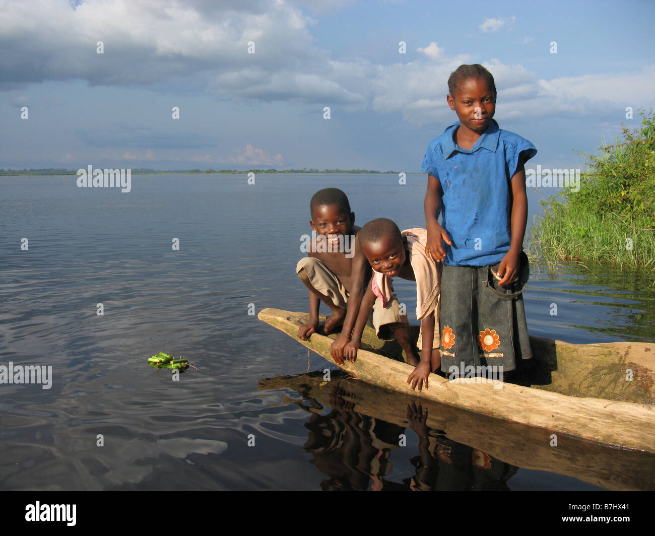 Tre giovani felici i bambini in una piroga sul fiume Congo a giocare con un giocattolo zattera Repubblica Democratica del Congo Foto Stock