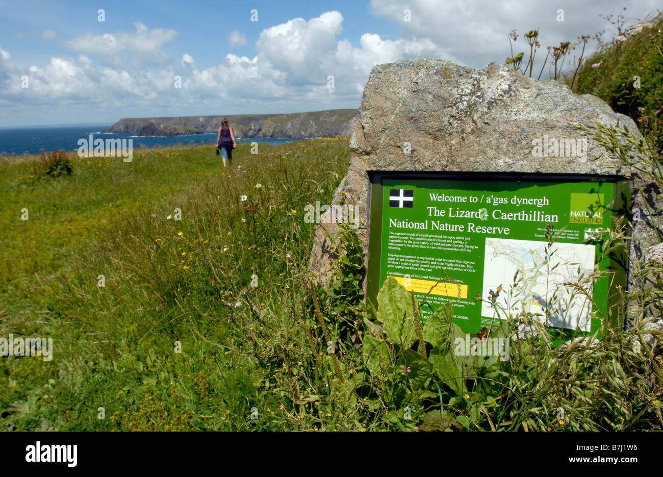 La penisola di Lizard, Cornwall, Inghilterra. Una donna cammina lungo il sentiero costiero con segno foreround. Foto Stock