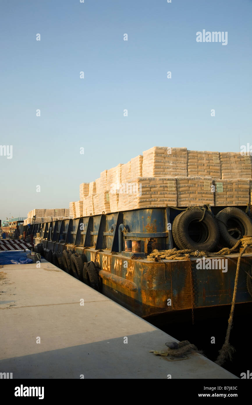 Importazione, operai lo scarico dei pallet di cemento iraniano, erogata dalla chiatta. presso la banchina di Al Sharjah, Dubai, UAE Foto Stock