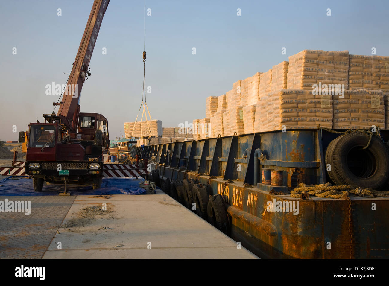 Importazione di materiali da costruzione, operai che scaricano pallet di cemento iraniano, consegnati da chiatta alla banchina di al Sharjah, Dubai, Emirati Arabi Uniti Foto Stock
