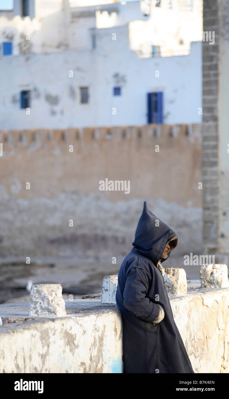 Un uomo è in piedi di fronte della medina di Essaouira indossando un djellaba tradizionale. Foto Stock