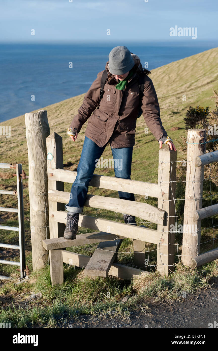 Una donna che cammina lungo il Ceredigion sentiero costiero attraversando un di legno stile West Wales UK Foto Stock
