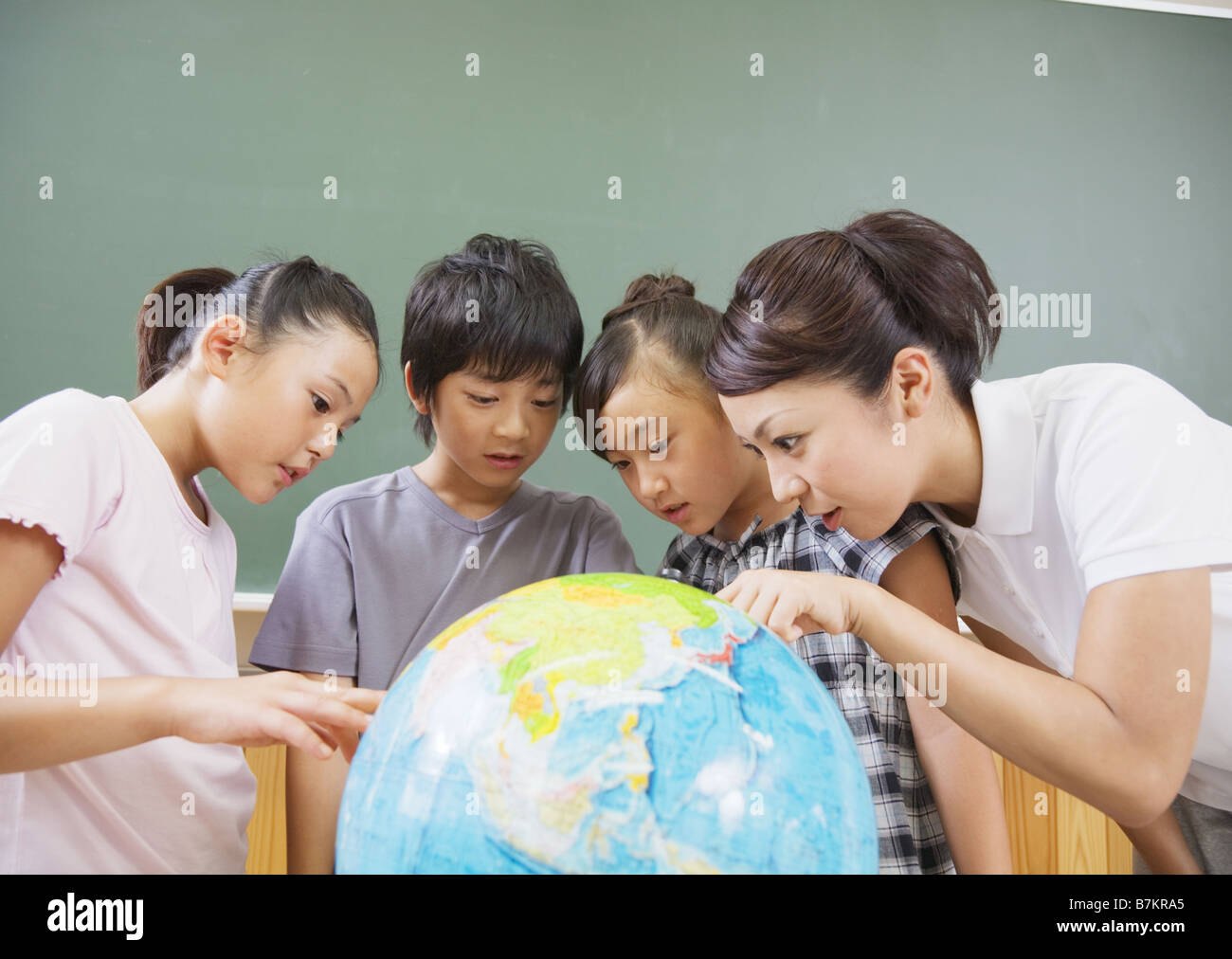Gli studenti elementari e il maestro guardando il globo terrestre Foto Stock