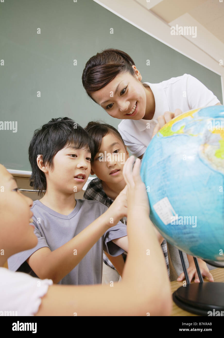 Gli studenti elementari e il maestro guardando il globo terrestre Foto Stock