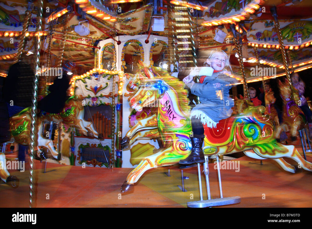 Bambino sfocata equitazione tradizionale illuminato Merry Go Round/giostra fairground ride, Winter Wonderland, Hyde Park, London, Regno Unito Foto Stock