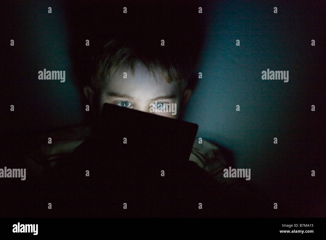 Bambino di nove anni giocare con il nintendo ds portatile sistema di video gioco al buio, esprimendo grande concentrazione Foto Stock
