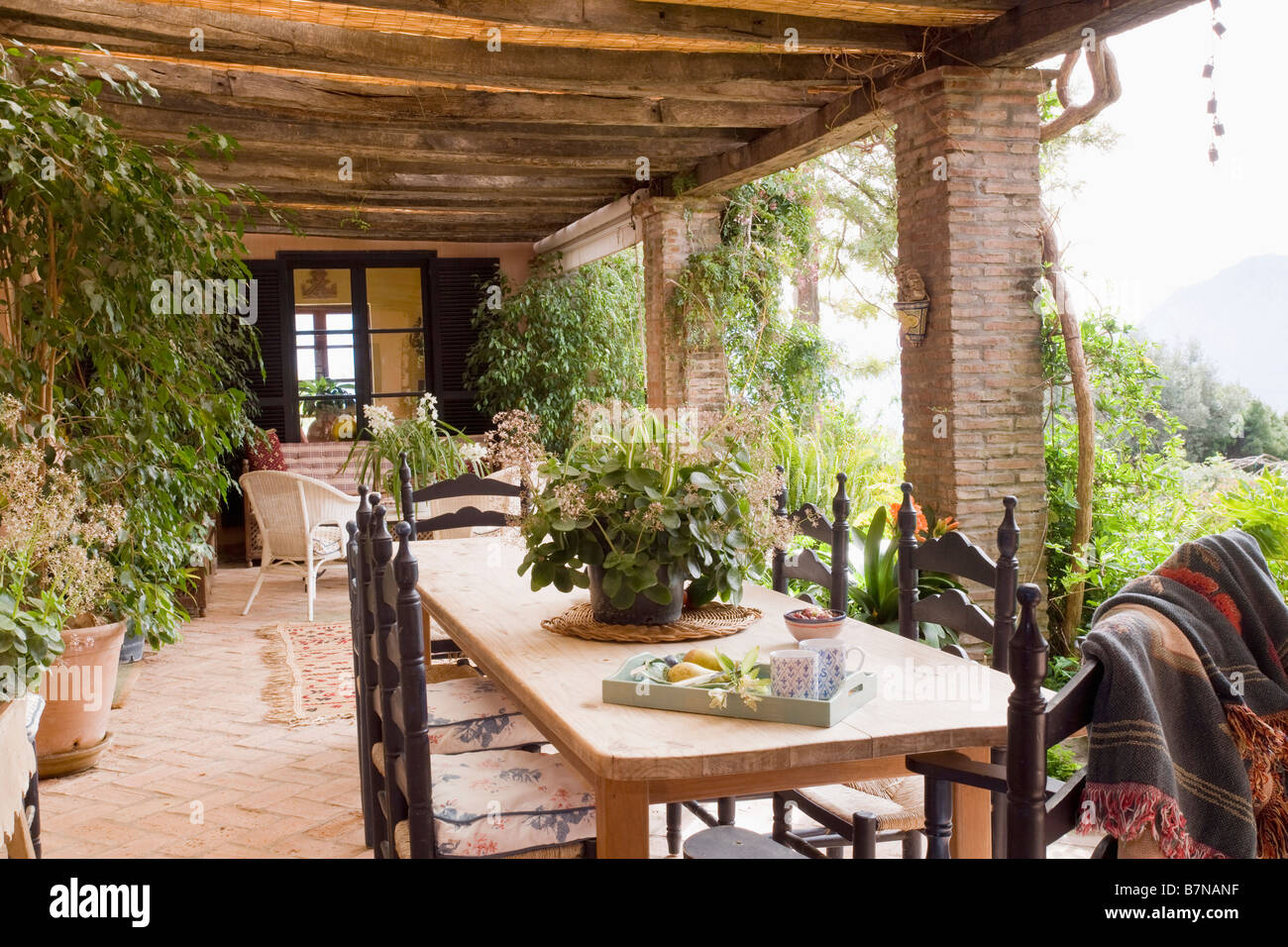 Tavolo in legno e sedie incise sulla veranda della villa spagnola con lussureggianti houseplants Foto Stock