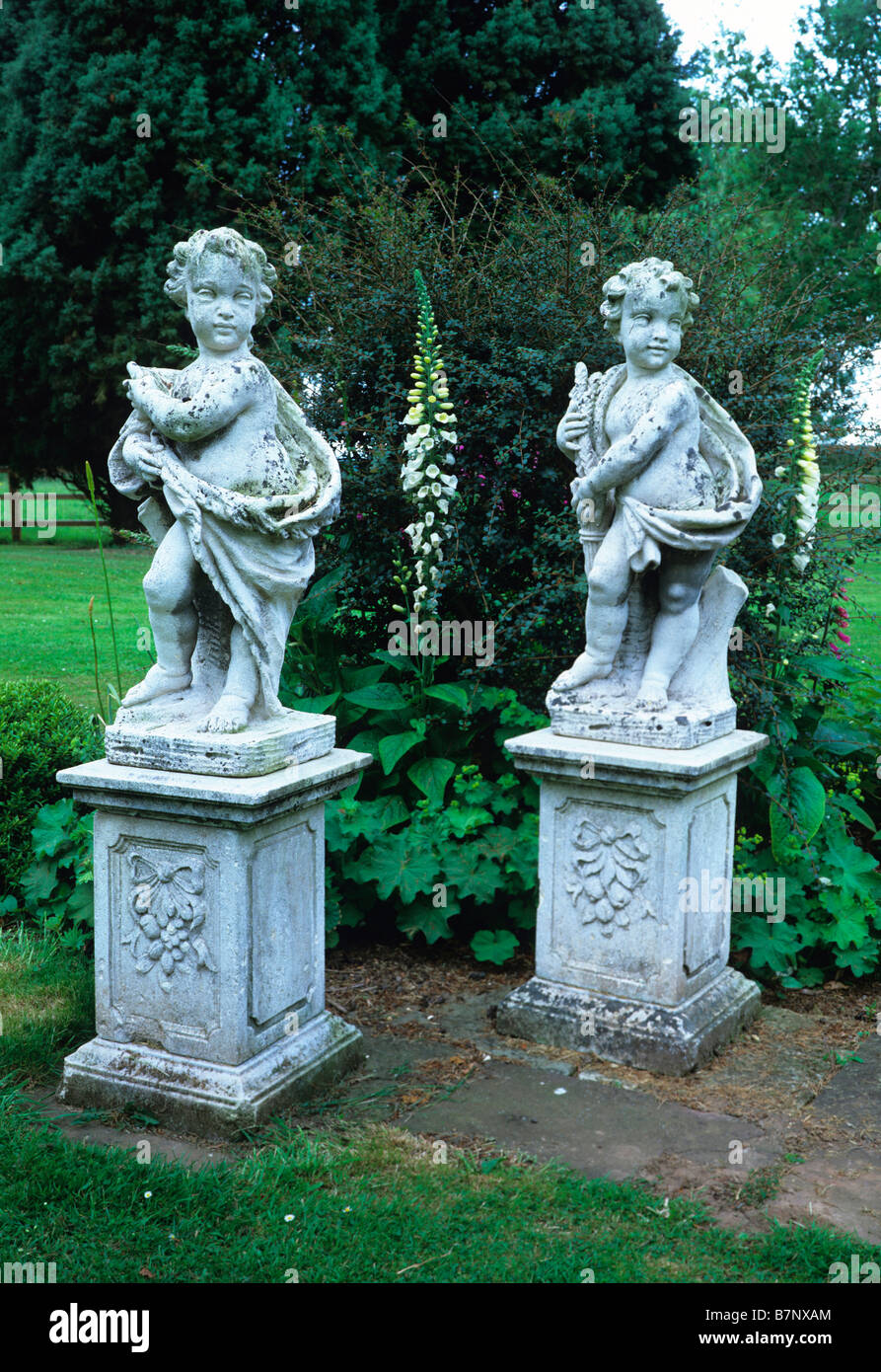 Twin putti in pietra su plinti con foxgloves bianco in un paese giardino Foto Stock