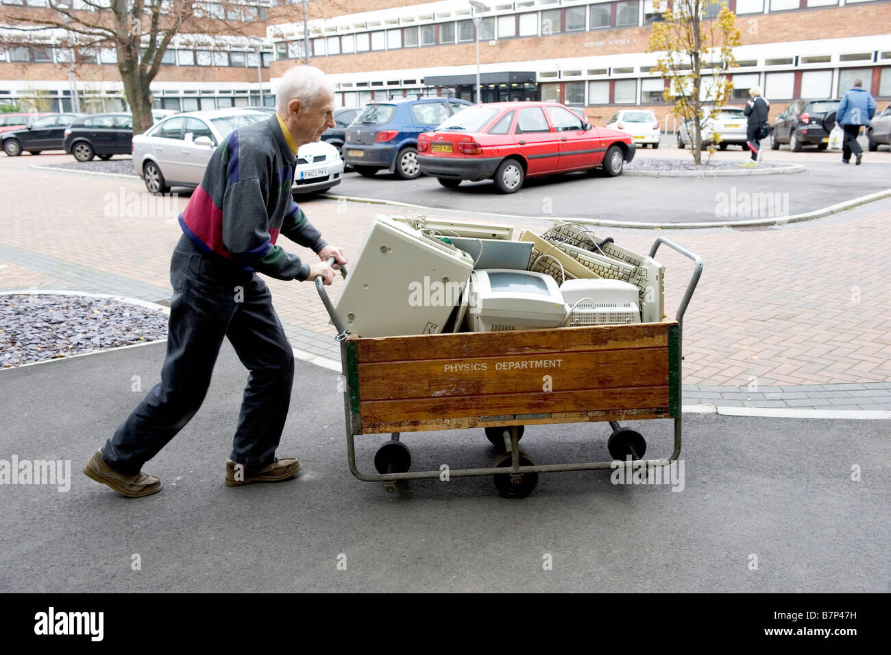 Un uomo anziano in un campus universitario spinge alcuni vecchi computer in un carrello in legno contrassegnati dipartimento di fisica Foto Stock