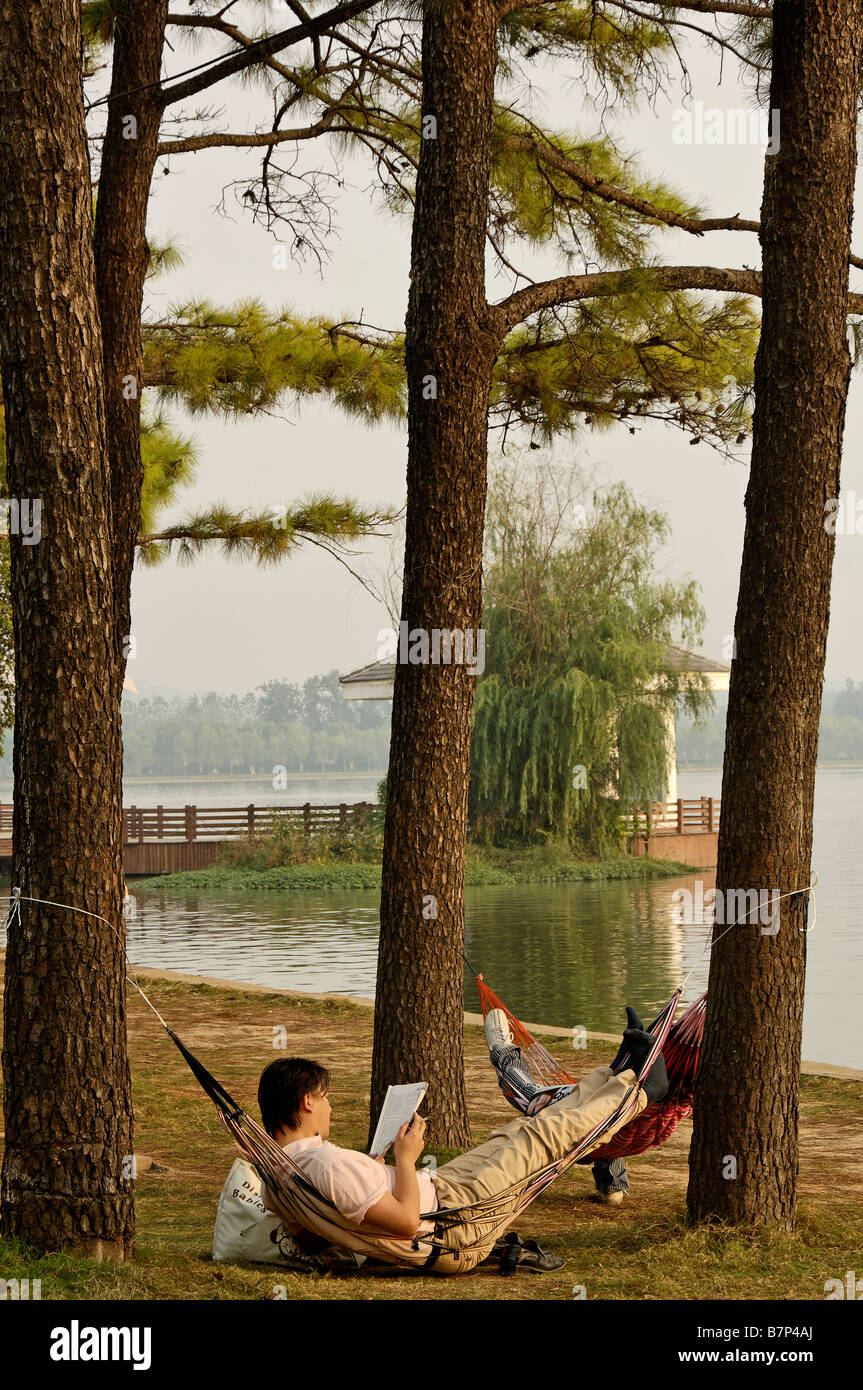 L'uomo la lettura di libro in amaca, Lago Xuanwu Nanjing Cina Foto Stock