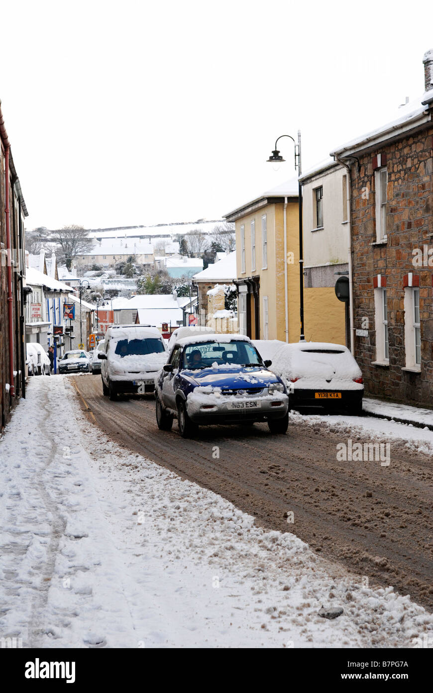 Cars driving attraverso un pieno di neve village street in cornwall, Regno Unito Foto Stock