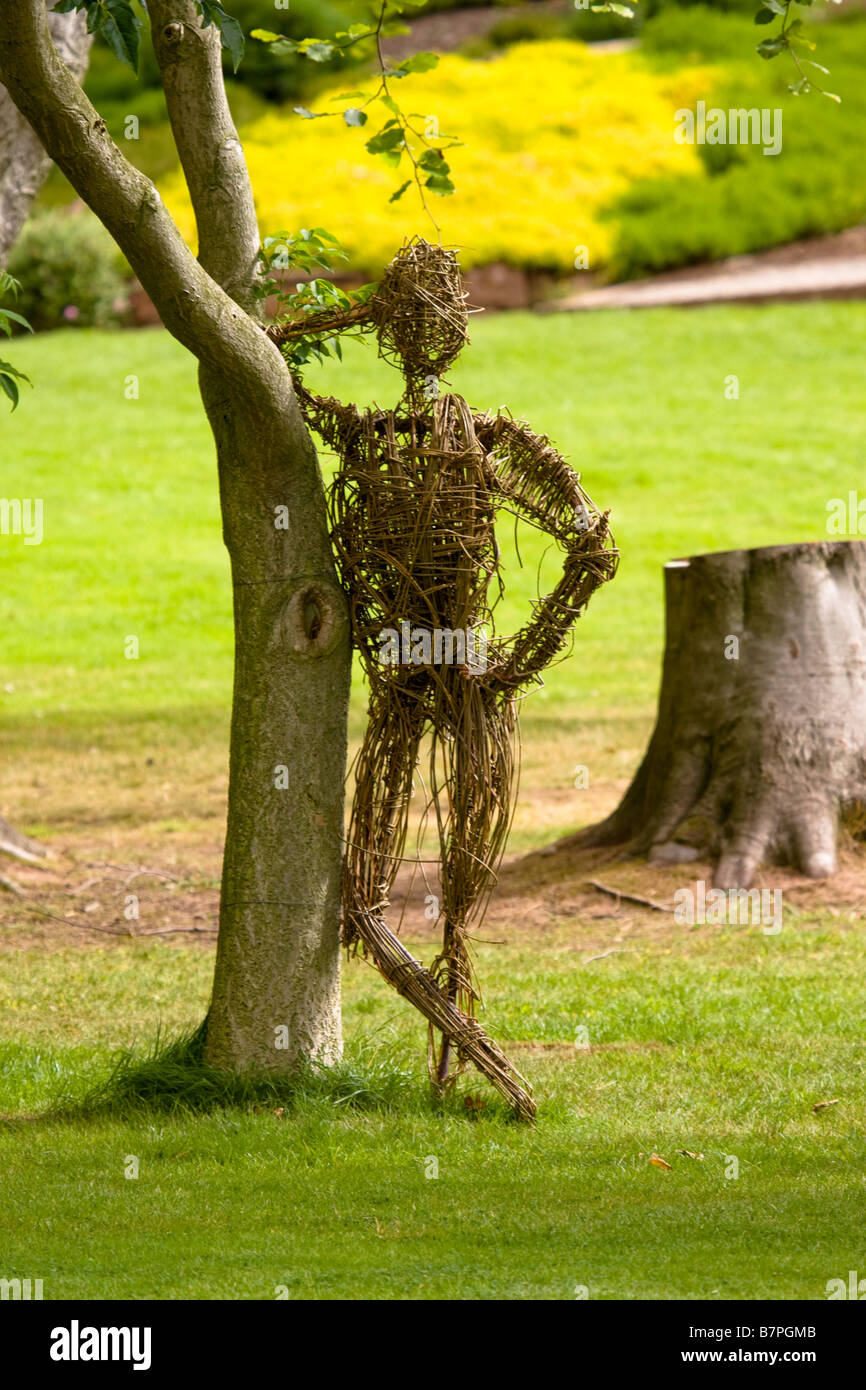 Una statua di vimini di un uomo appoggiato a un albero, Ness giardini, Wirral Foto Stock