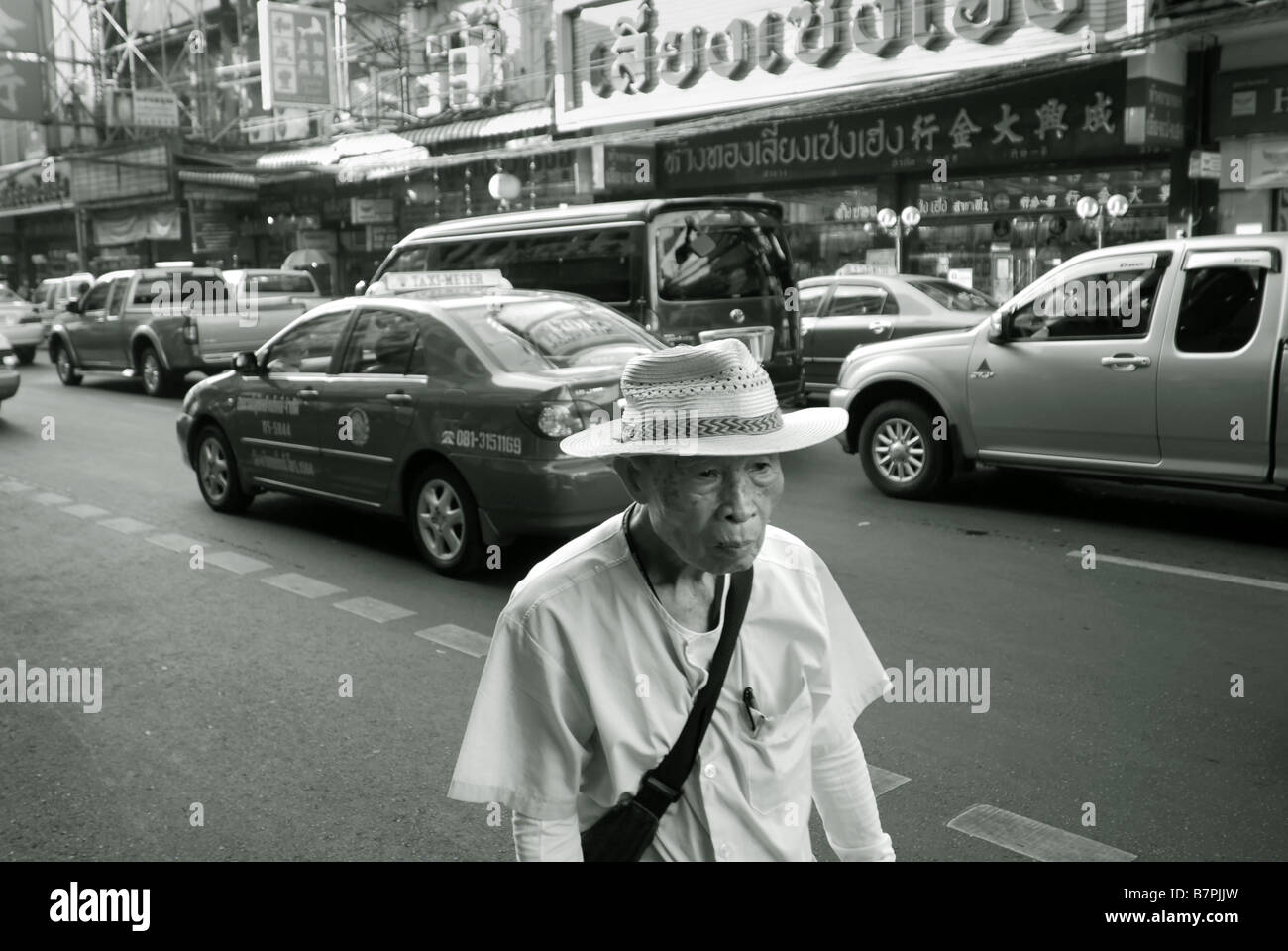 Il vecchio uomo che cammina sulla strada accanto a traffico pesante lungo Thanon Yaowarat in Chinatown Bangkok in Thailandia Foto Stock