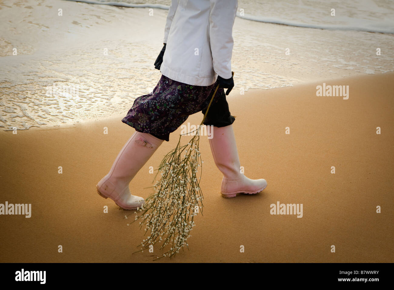 Donna che mantiene il ramo camminando sulla riva del mare in prossimità delle gambe Foto Stock