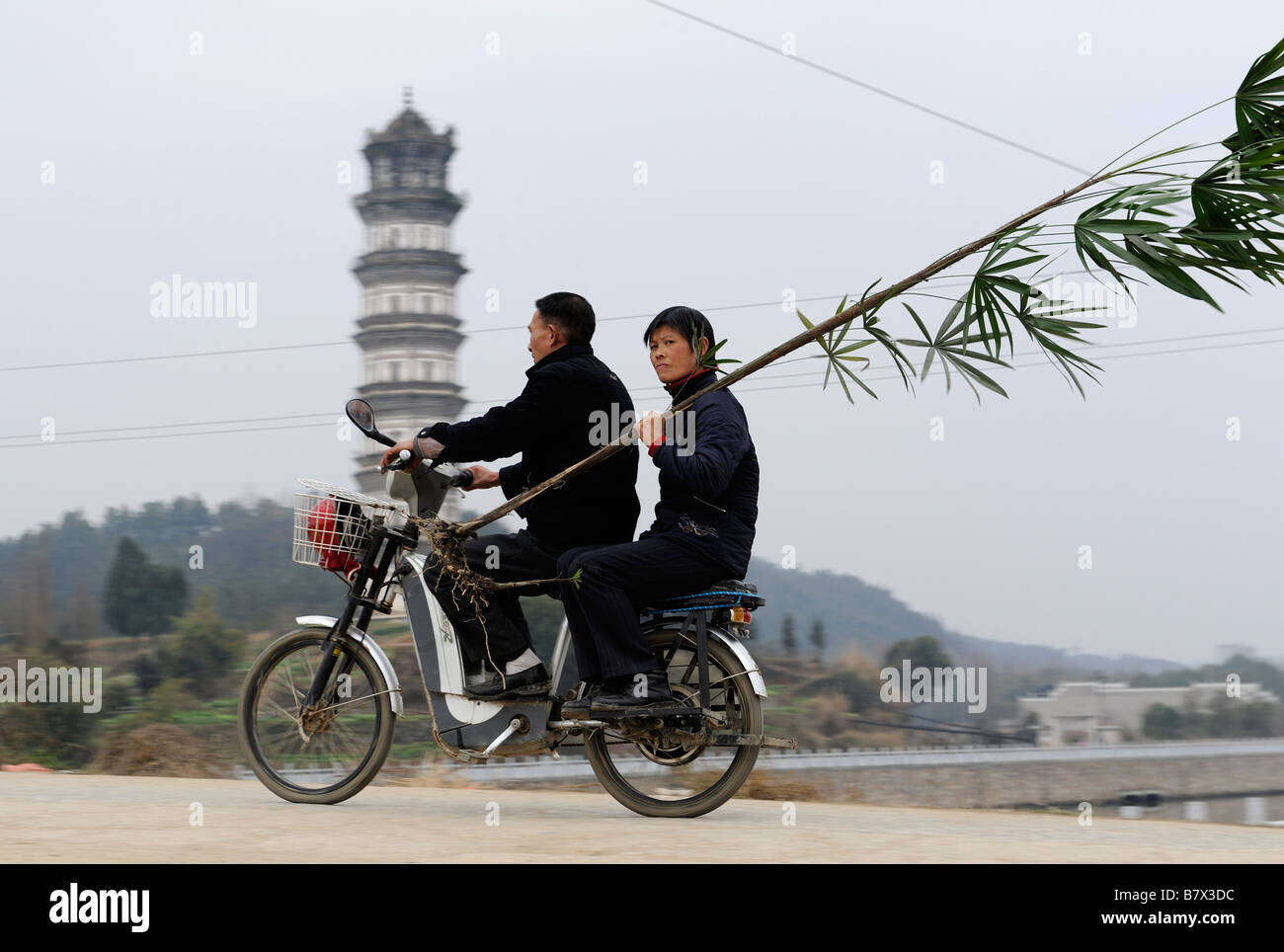Un uomo cinese aziona un motore elettrico il moto con una signora passato un antico pagoda in Yifeng, Jiangxi, Cina. 02-Feb-2009 Foto Stock