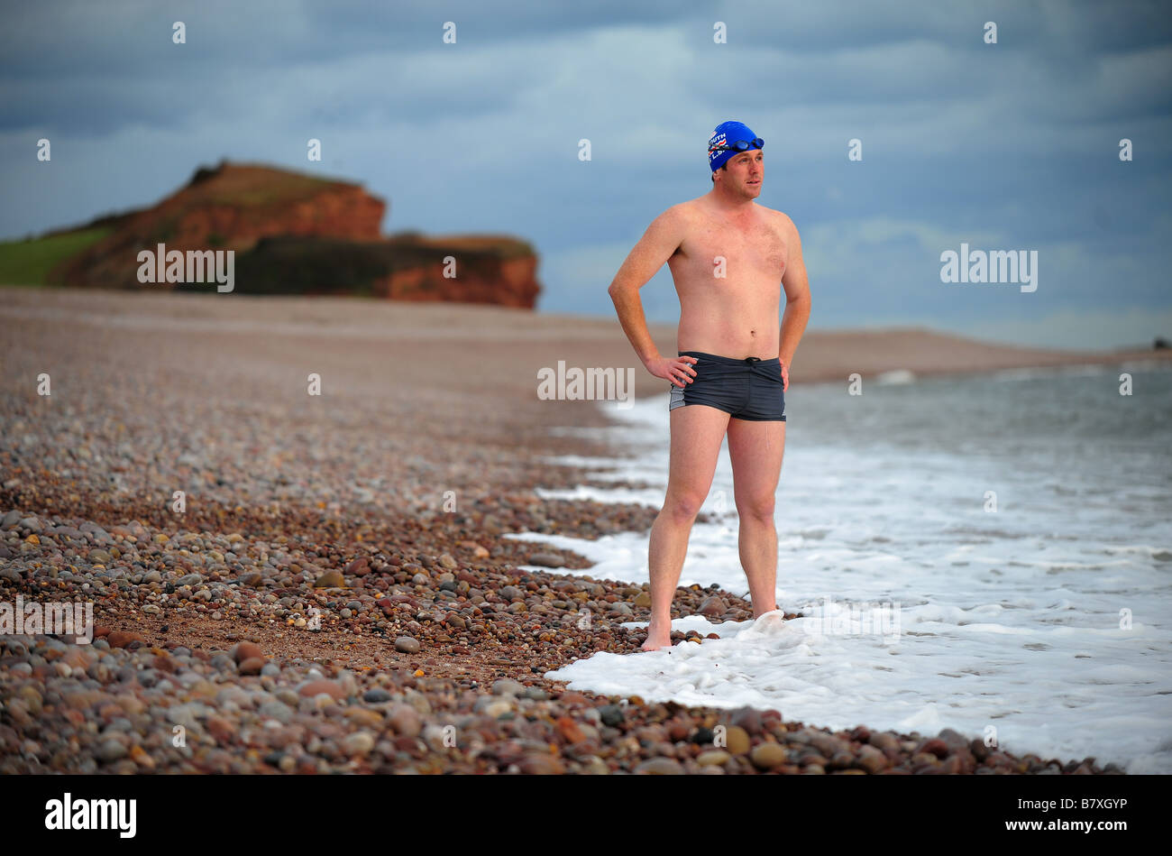 Un uomo si prepara per andare a nuotare indossando una cuffia per la piscina e gli occhiali sulla spiaggia a Budleigh Salterton. Foto Stock