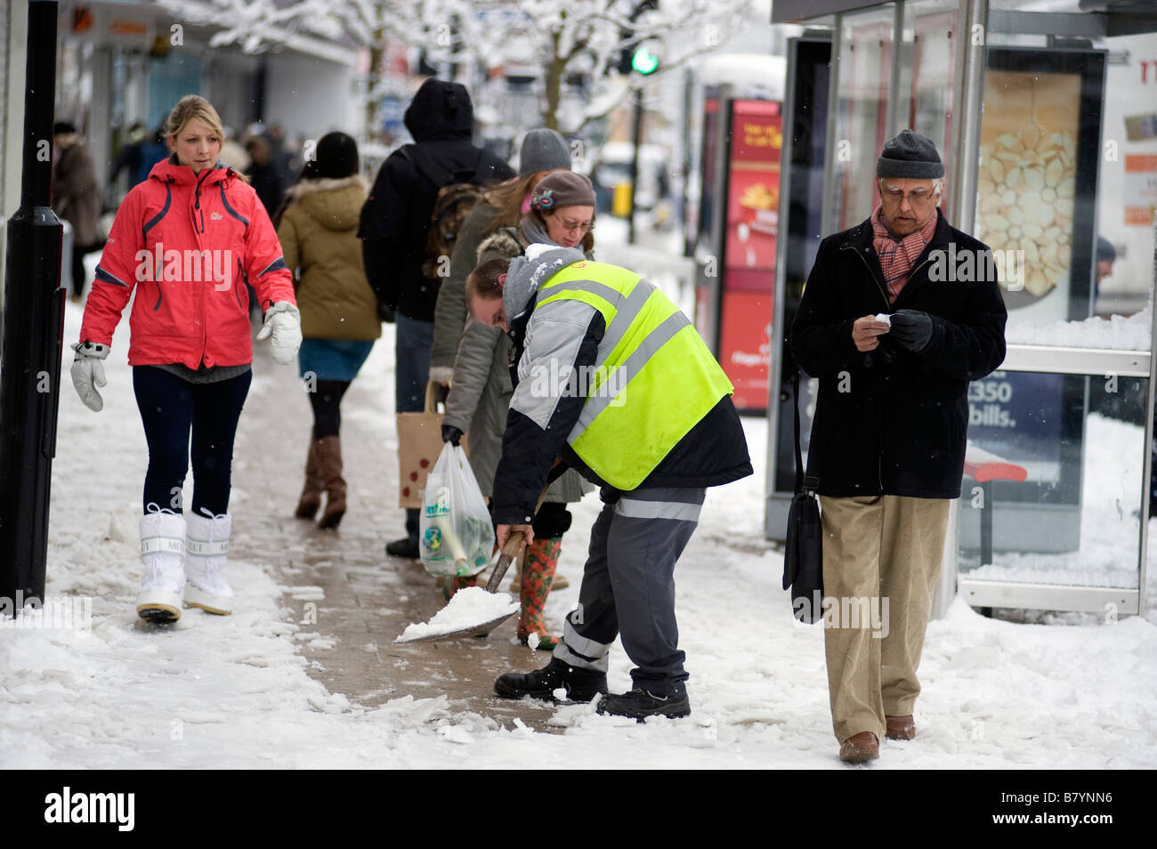 Un lavoratore del consiglio spalare la neve da una trafficata zona pedonale high street Foto Stock