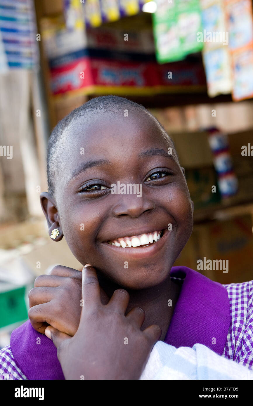 Giovane ragazza nigeriana ha appena fatto ritorno da scuola ed è pronto per aiutare la madre sulla famiglia in stallo su un mercato locale Foto Stock