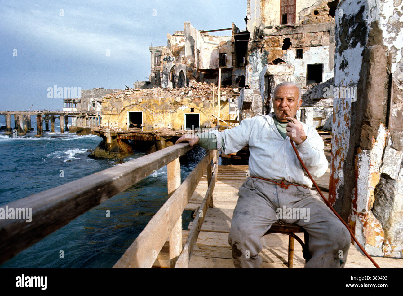 Vecchio Beirut, Libano presi subito dopo la guerra civile conclusa intorno al 1990. Uomo seduto sul lungomare tra edifici in rovina. Foto Stock