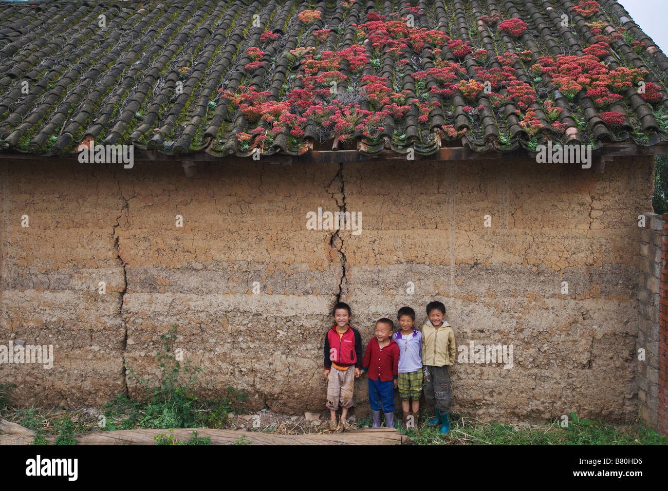 I bambini e la casa di villaggio con tetto di tegole coperte da colorati moss nella provincia dello Yunnan in Cina Foto Stock