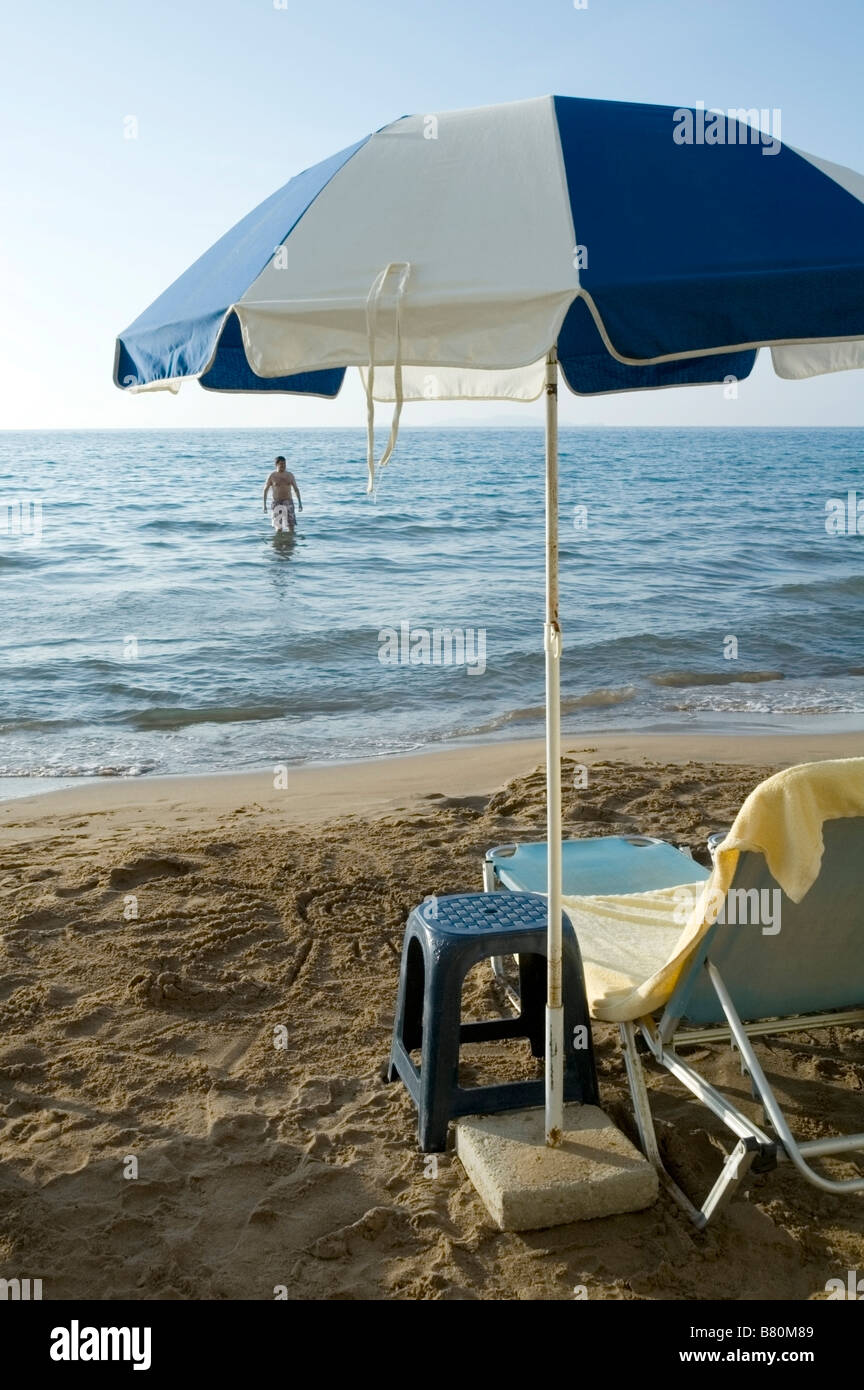 Uomo in mare Ionio e una sun lounge sulla spiaggia con ombrellone e tavolo, Sidari litorale Nord Corfu, Grecia, UE Foto Stock