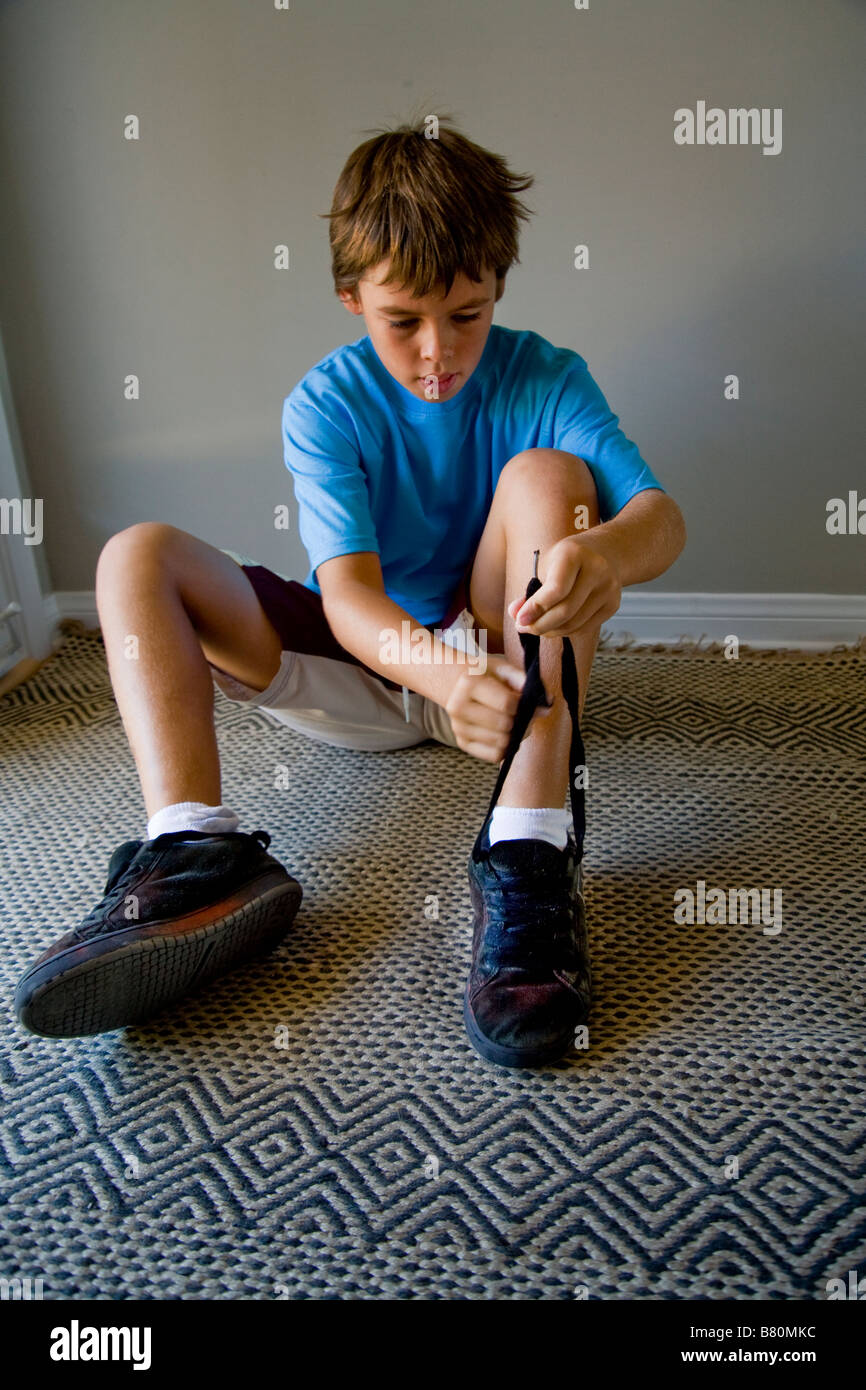 Seduto sul pavimento mediante la porta anteriore a 10 anno vecchio ragazzo lacci le sue scarpe a casa in Laguna Niguel CA Foto Stock