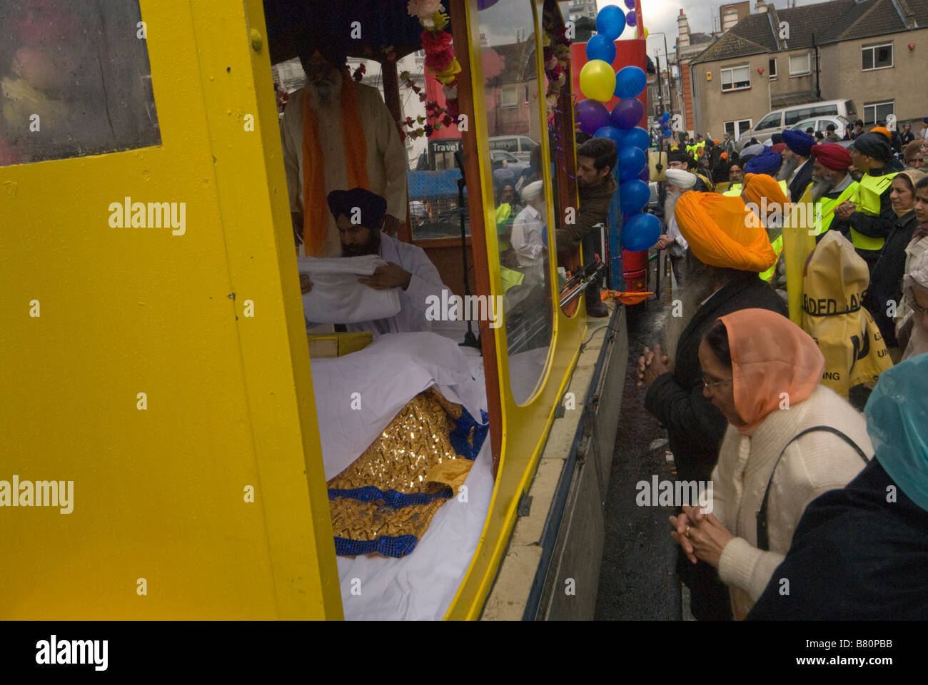 I sikh guarda con riverenza come il Guru Granth Sahib è installato sul galleggiante per la processione Vaisakhi a Woolwich, Londra Foto Stock