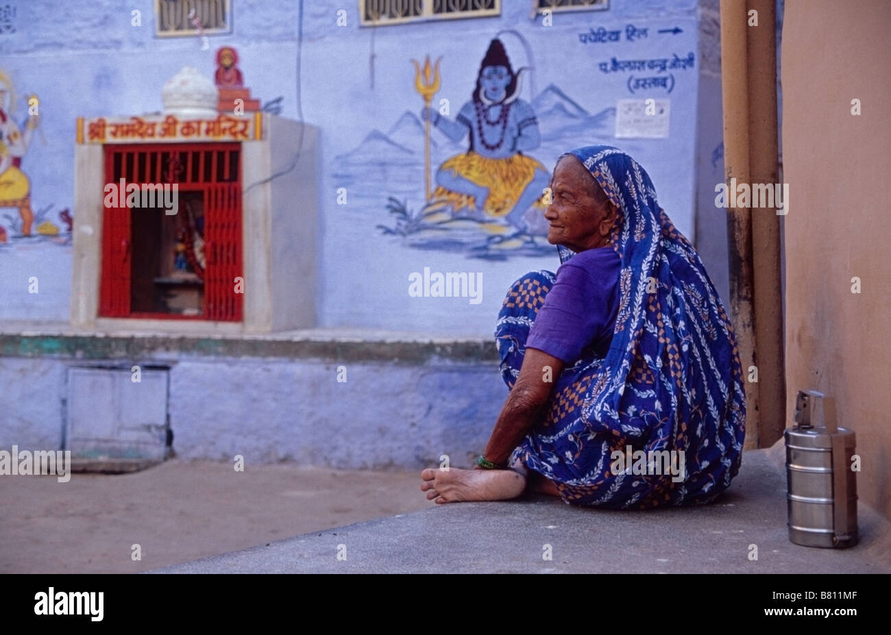 Una donna seduta vicino a un santuario dedicato al dio Rama in Jodhpur la città blu ( sulla parete: un murale di shiva ) Foto Stock