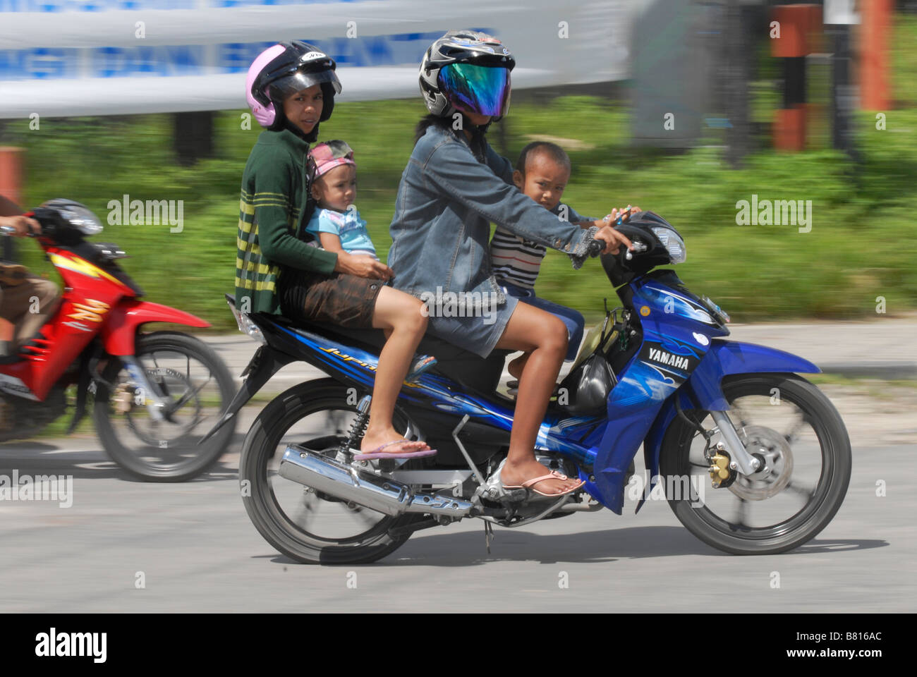 Motociclo con una donna che indossa un casco e quattro figli senza casco di Biak, Indonesia. Foto Stock