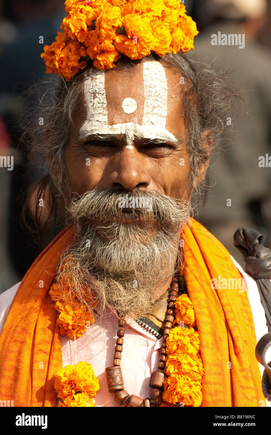 Faccia foto ritratto di un Sadhu nepalese vestito in arancione vesti, con la faccia di vernice e fiori nei capelli nel cuore di Kathmandu, Nepal Foto Stock