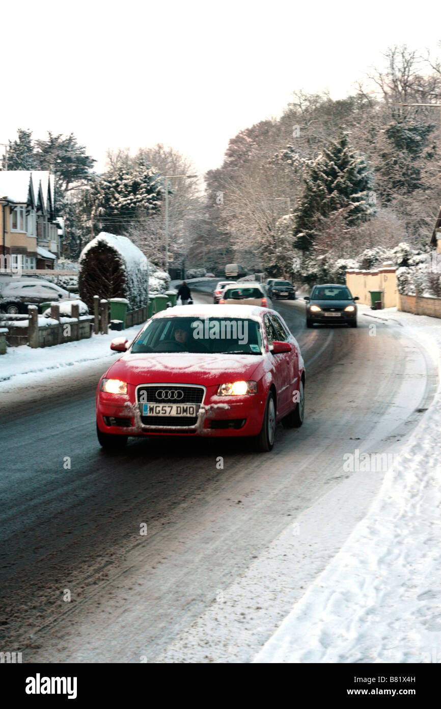Un rosso Audi auto guidare lentamente il lungo Berkley Road, dopo una caduta di neve a Frome, Somerset, Inghilterra Foto Stock